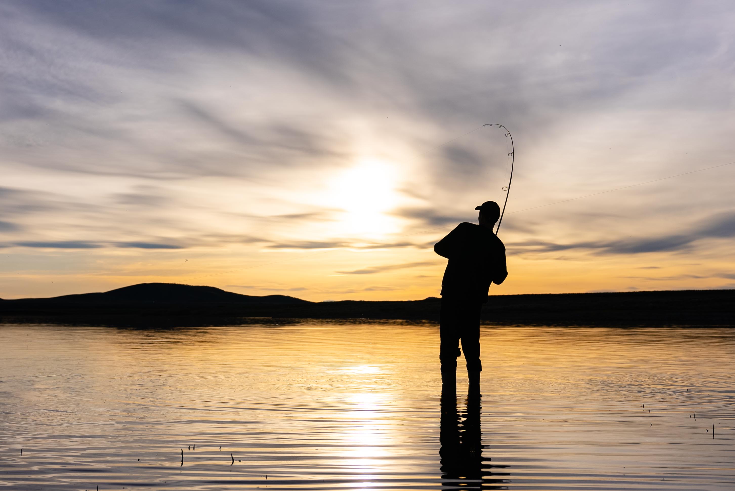 Carl, hooked into a fish, looking out over a sunset.